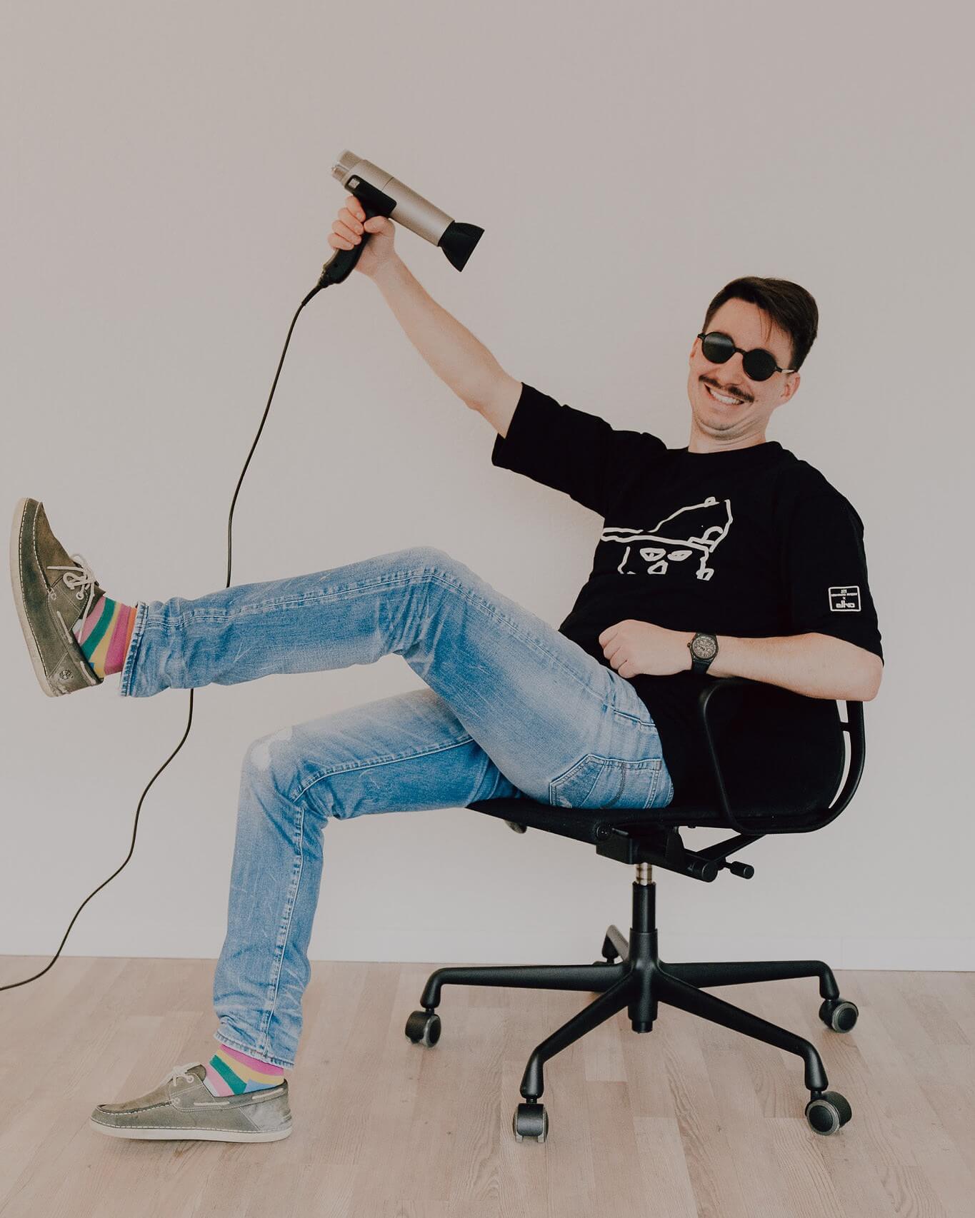 Hairdesigner Ray aus Zürich sitzt locker auf dem Stuhl und föhnt die Haare.